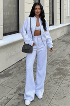 Woman wearing The Voyager Zip Set light gray zip-front sweatshirt and wide-leg joggers with sneakers and a black shoulder bag walking outdoors