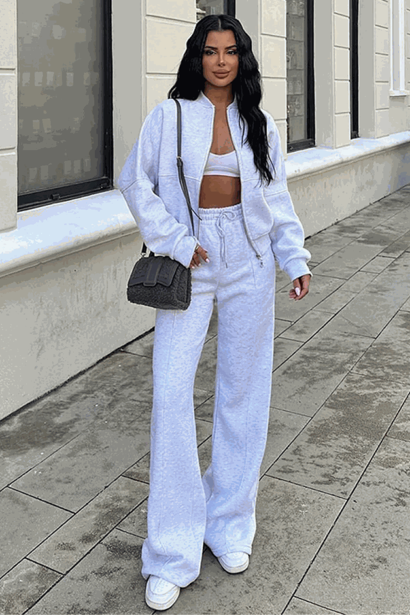 Woman wearing The Voyager Zip Set light gray zip-front sweatshirt and wide-leg joggers with sneakers and a black shoulder bag walking outdoors