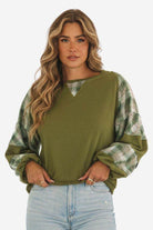 Green waffle knit sweatshirt with plaid sleeves and v-notch neckline worn by woman with wavy hair