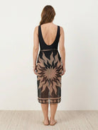 Woman wearing a deep-V swimsuit with ruched bust and waist, paired with a sheer wrap sarong tied at the hip.