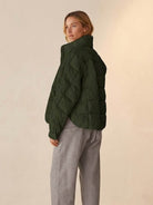 Woman wearing olive green lightweight puffer travel jacket with quilted design and high collar, paired with gray pants.