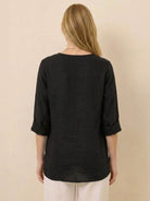 Back view of a woman wearing a black Pure Linen Age-Defying Button Detail Shirt with rolled-up sleeves.