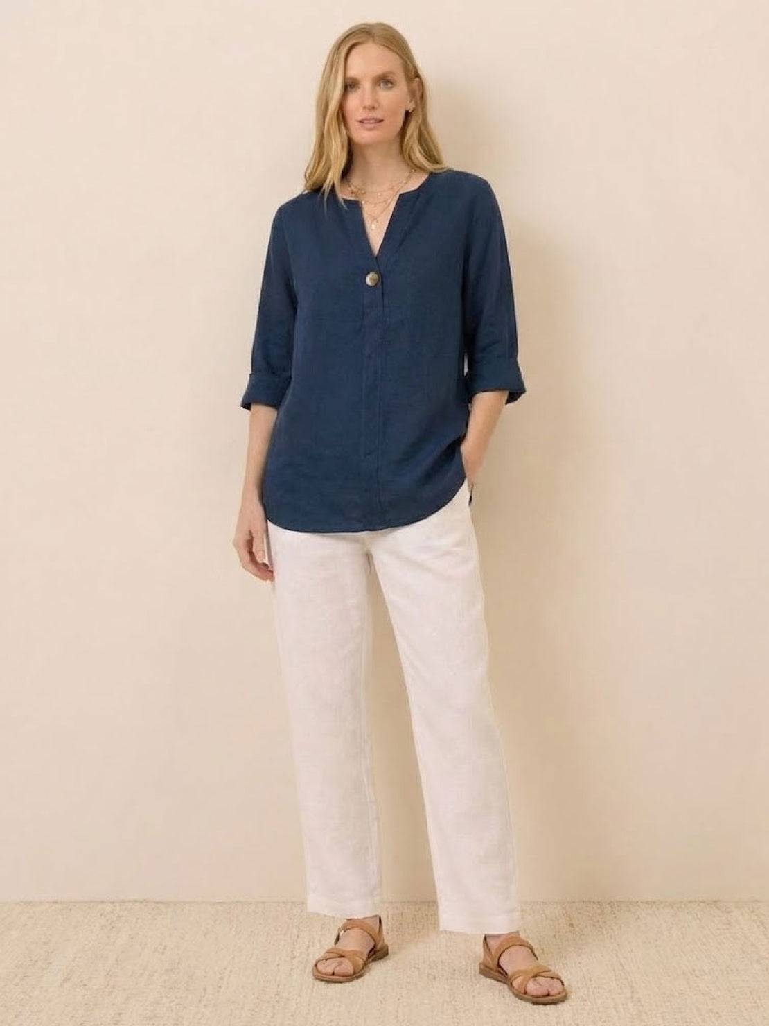 Woman wearing navy Pure Linen Age-Defying Button Detail Shirt with white pants and sandals against neutral background