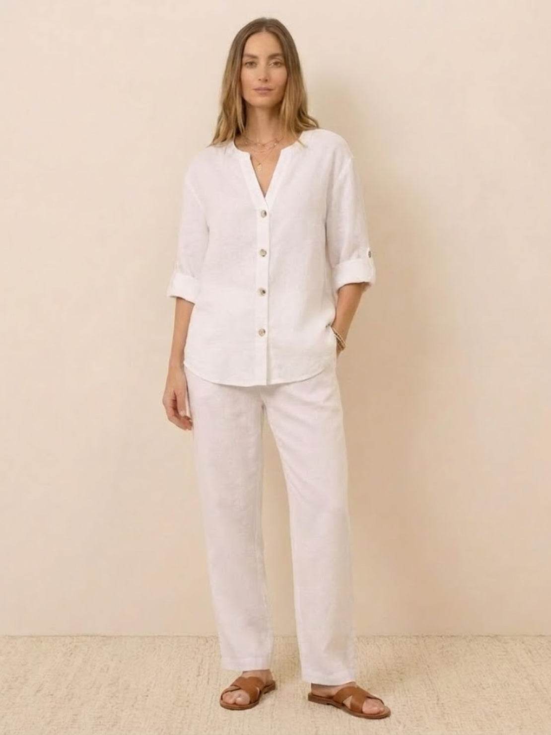 Woman wearing a white pure linen age-defying button detail shirt and matching linen pants with brown sandals.