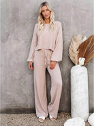 Woman wearing a beige round neck loose fit cozy two-piece set with wide-leg pants against gray textured wall