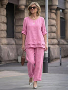 Woman wearing pink asymmetrical two-piece trouser set with rolled sleeves and loose fit walking outdoors