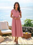 Woman wearing a capped-sleeve voluminous pleated midi dress with flowing skirt and pockets