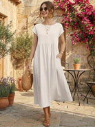 Woman wearing a capped-sleeve voluminous pleated midi dress with flowing skirt and pockets