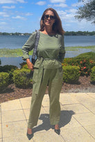 Woman wearing olive green cotton-linen monochrome relaxed longline top and wide-leg pants outdoors by a lake.