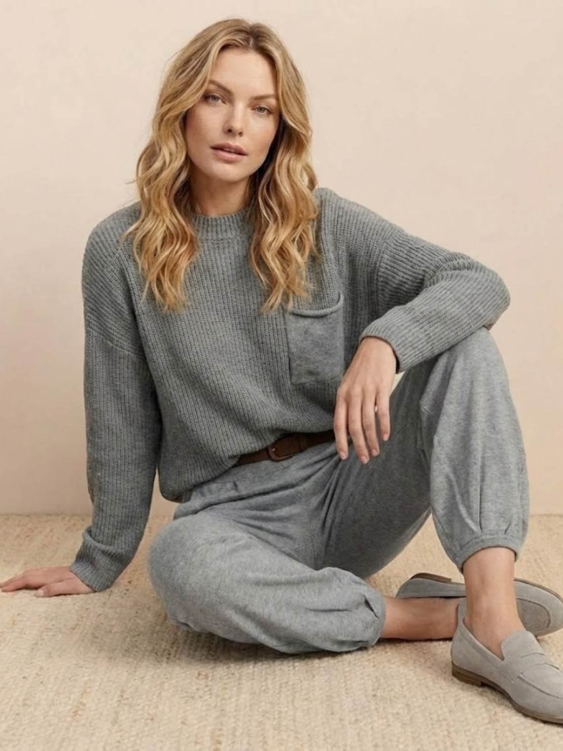 Woman wearing European Minimalism relaxed gray knit sweater top and trouser set sitting on floor