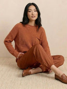 Woman wearing European minimalism relaxed sweater and trouser set in rust color sitting on floor