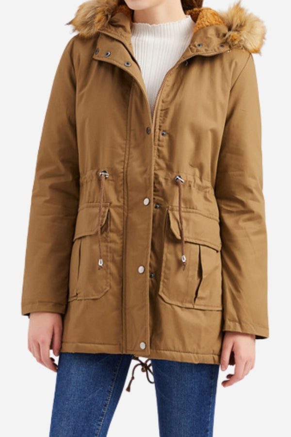Woman wearing a brown large hooded velvet coat with fur trim and front pockets.