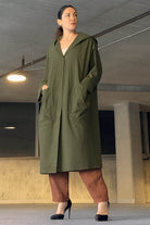 Woman wearing oversized green water resistant windbreaker with hood and front pockets in an indoor setting