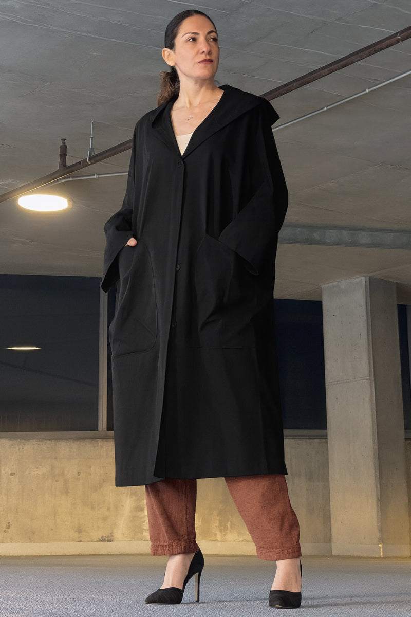 Woman wearing oversized black Heritage Windbreaker Jacket with hood and snap-button closure in urban setting