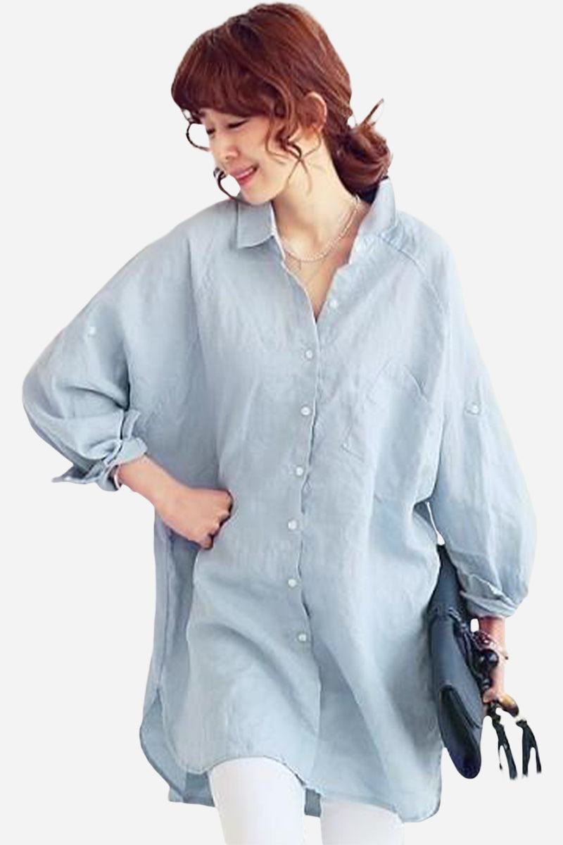 Woman wearing a light blue oversized linen shirt with loose sleeves and button-down front holding a black clutch.