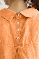 Close-up of the back collar and buttons on an oversized linen shirt in burnt orange color