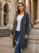 Oversized long zip sweatshirt hoodie in dark gray with drawstring hood and large front pockets worn by woman outdoors