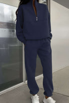 Woman wearing navy cotton blend tracksuit with zip neckline and relaxed fit pants.