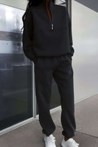 Black cotton blend tracksuit with zip neckline and relaxed fit worn with white sneakers