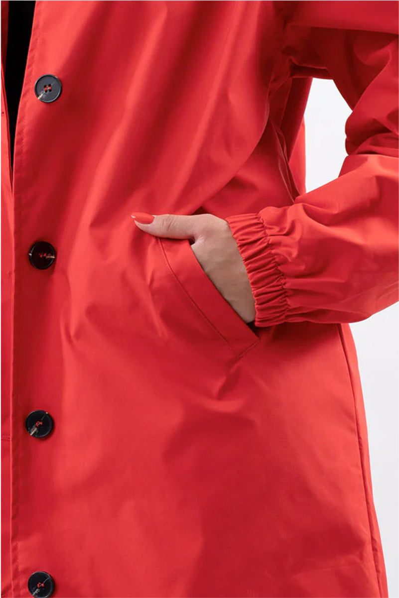 Close-up of a red Rain Couture Windbreaker with button details and elastic cuffed sleeve showing hand in pocket