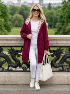 Woman wearing burgundy Rain Couture Windbreaker with floral hood lining, white outfit, sunglasses, and white handbag outdoors