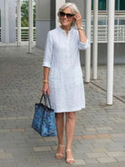 Woman wearing white knee-length cotton dress with rolled ¾ sleeves and carrying blue handbag outdoors