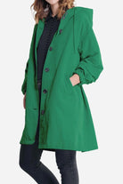 Woman wearing green oversized Rain Couture Windbreaker with hood and buttons over black outfit
