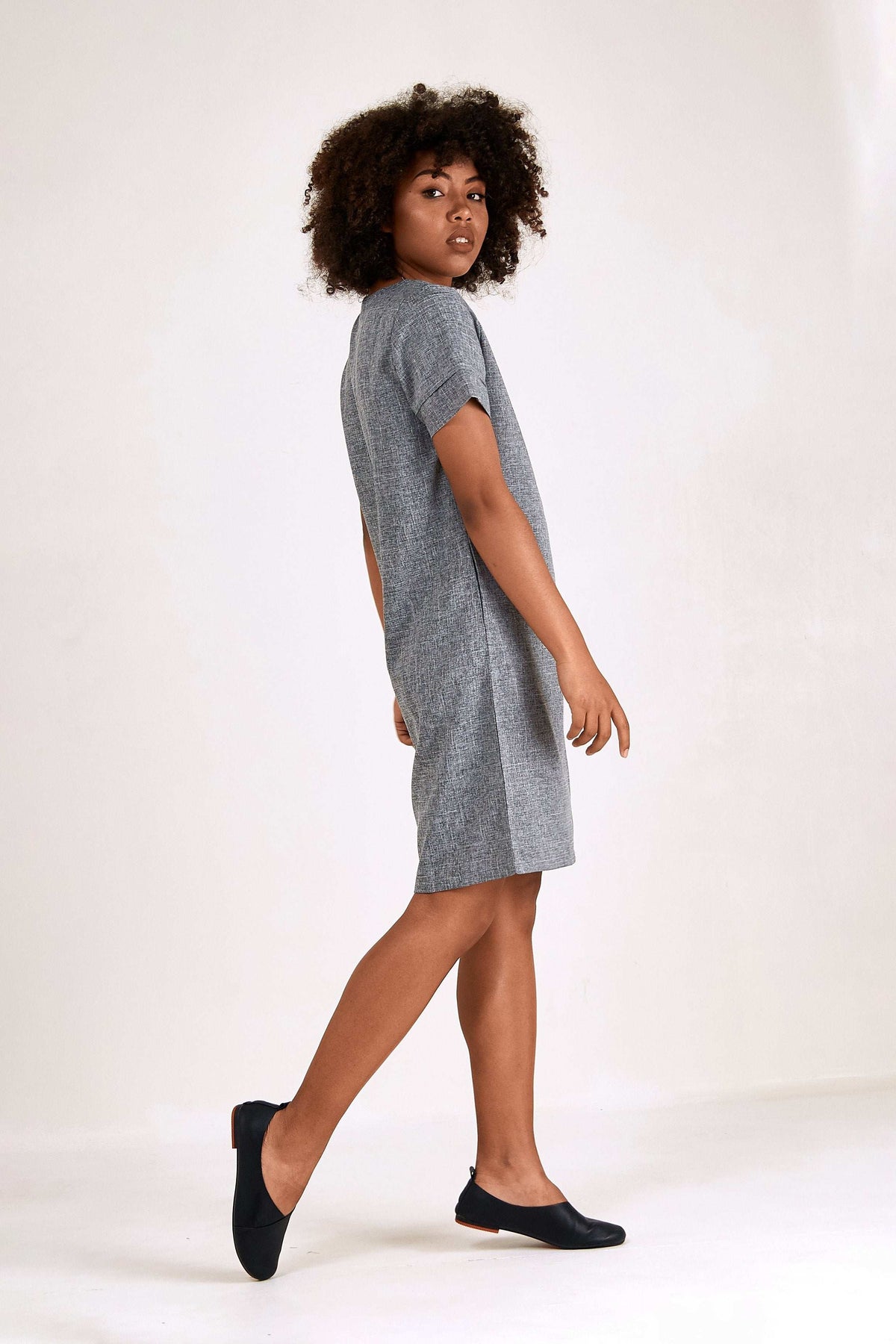 Woman wearing a grey short sleeve shift dress with round neck and side pockets, knee-length style